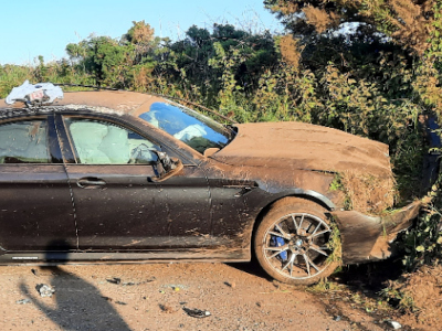 Photo of the crashed BMW, covered in soil and embedded in a hedge.